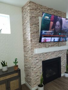 A beautifully remodeled fireplace with a brick accent wall and a mounted flat-screen TV above, flanked by potted plants, showcasing the final touch in a cozy living room renovation.